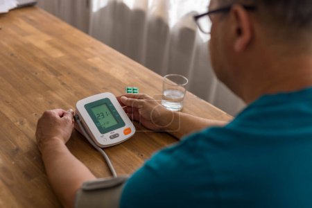 Seniory man checks blood pressure with monitor on upper arm in room smiling elderly gentleman measures blood pressure at home monitoring his health,. High quality photo