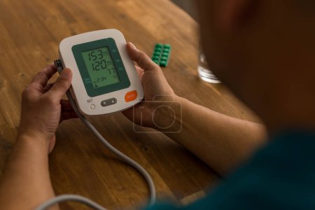 Seniory man checks blood pressure with monitor on upper arm in room . High quality photo