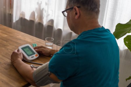 Seniory man checks blood pressure with monitor on upper arm in room . High quality photo