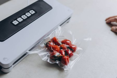 a mans hand is using a vacuum machine to vacuum pack strawberries into plastic bags. . High quality photo