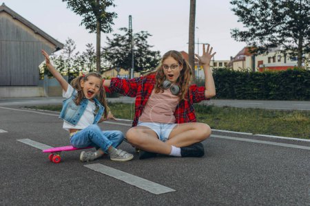 Two teenage girls sitting on a skateboard and smiling at the camera. High quality photo