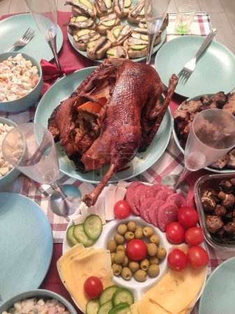 Téléchargez les photos : Table de fête avec poulet de canard entier et assiettes turquoise tranchant saucisse fromage viande verres vacances dîner de famille, olives - en image libre de droit