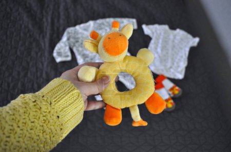 yellow toy giraffe rattle for children in hand. white children's clothing on a gray background. yellow sweater