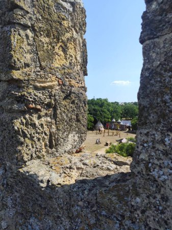 Blick aus dem Fenster einer Festung, Burg, Turm auf den Wiesen, Gras, Himmel. Steinturm, Turmspitze, antike Burg, altes, steinernes Haus. Mittelalterliches Ritterturnier