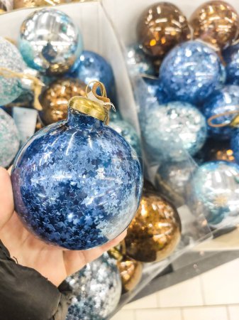 2025, blau-goldene Weihnachtskugel mit Sternen in den Händen und vielen Kugeln in einer Schachtel. Weihnachtskugeln im Geschäft kaufen
