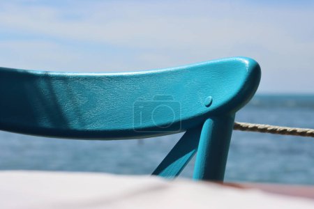 Photo for Closeup of the retro chair back detail. Beautiful wooden texture of turquoise painted vintage chair back. Scenic blue sky and sea view on the background.  Sunny summer day on Adriatic. Selective focus - Royalty Free Image