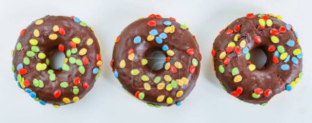 Photo for Set of three tasty chocolate donuts with smarties on white background. 3 Doughnut decorated with colorful candies on top. Birthday party.  Hanukkah celebration concept. Isolated. Top view - Royalty Free Image