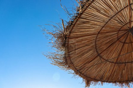 Photo for Albania. Durres. Closeup of the straw sun umbrella on the Adriatic beach. A beautiful sunny day and the blue sky on the background.  Straw texture. Copy space. Selective focus. - Royalty Free Image