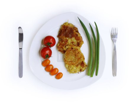 Homemade fried grated potato pancakes served with fresh tomatoes and green onions on the white plate, fork and knife. Draniki. Top view. Cutout and isolated with clipping path on the white background