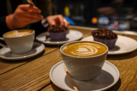 Photo for Copenhagen, Denmark - February, 20th, 2023. Espresso House. A cup of cappuccino with milk foam and delicious homemade chocolate cupcake on the vintage wooden table. Selective focus - Royalty Free Image