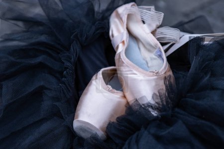 Photo for Closeup of the pink ballet pointe shoes laying on the black chiffon Tutu. Two beige ballet slippers on the dark background. Minimalistic concept. Copy Space. Selective focus. - Royalty Free Image
