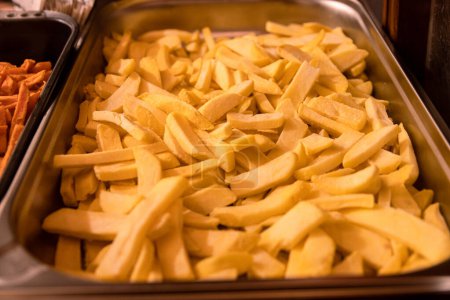 Photo for Yummy French fries in the metal tray. Potato chips on the counter at the street market. Selective focus. Side view. Bokeh. - Royalty Free Image