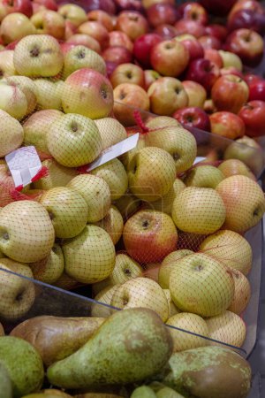 Photo for Fresh pears and apples in red shopping net. Fruits arranged in the grocery store on the counter. Green pears, apples with producer tags stickers on food market rack. Side view. Selective focus. - Royalty Free Image