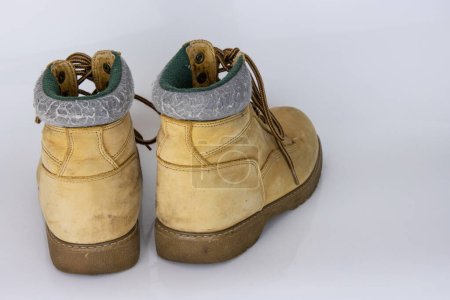 Paire de vieilles bottes de randonnée en dentelle jaune usées Isolé sur une surface blanche brillante avec un bel effet de réflexion. Chaussures de marche touriste d'occasion. Vue de derrière. Espace de copie. Fond blanc.