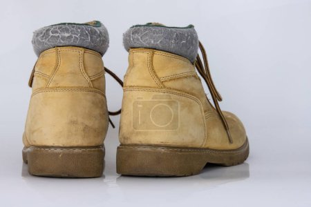 Paire de vieilles bottes de randonnée en dentelle jaune usées Isolé sur une surface blanche brillante avec un bel effet de réflexion. Chaussures de marche touriste d'occasion. Vue latérale. Espace de copie. Fond blanc.