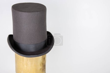 Magic hat. Topper. Elegant vintage gray beige wool felt top hat with black band on the wooden hat block. Grosgrain ribbon trim around rolled brim. Isolated on white background. Close-up. Copy space.