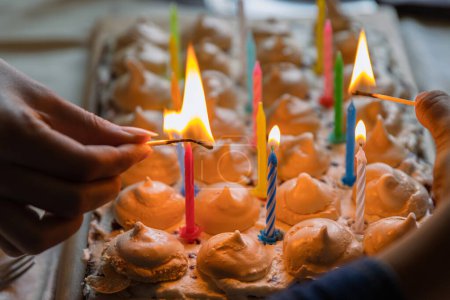 Photo for Hands of two people lighting colorful candles on the large homemade chocolate cake, decorated with meringues and whipped cream. Celebration party concept. Close-up. Selective focus. - Royalty Free Image