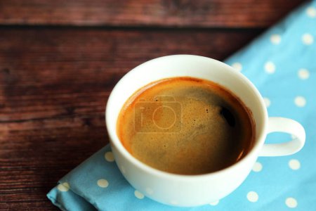 Una taza de café caliente en tela azul claro sobre mesa de madera, café expreso caliente.