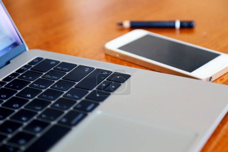 Ordenador portátil con teléfono inteligente y lápiz en la mesa de madera, trabajando a distancia.