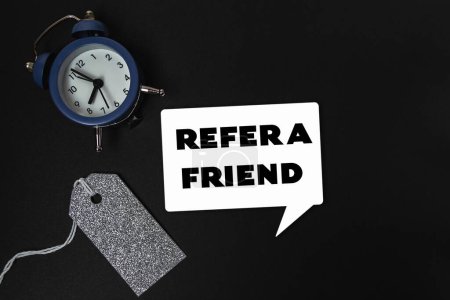 Photo for A clock sits on a table with a tag that says refer a friend. The clock is blue and white and has a black face - Royalty Free Image