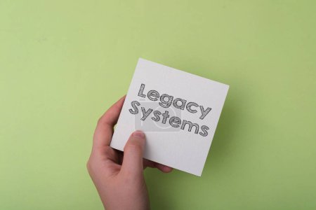 Foto de Una mano sosteniendo un pedazo de papel con la palabra Legacy Systems escrita en él. Concepto de transmisión de conocimientos y tradiciones de una generación a otra - Imagen libre de derechos