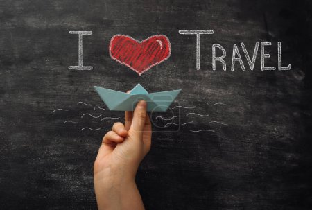Eine Hand hält ein Papierboot mit den Worten "Ich liebe Reisen" darauf geschrieben. Konzept von Abenteuer und Reiselust