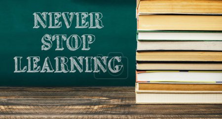 Never stop learning is written on a chalkboard with stacks of books behind it. The image conveys the idea that learning is a continuous process and should never be stopped