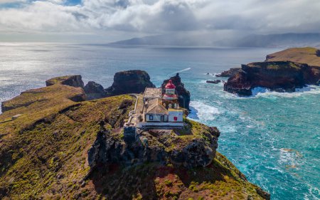 Lighthouse from aerial view at Sao Lourenco peninsula in Madeira. Farol da Ponta de So Loureno, Madeira. Lighthouse on a small island by the ocean with waves, clouds.