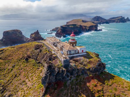 Lighthouse from aerial view at Sao Lourenco peninsula in Madeira. Farol da Ponta de So Loureno, Madeira. Lighthouse on a small island by the ocean with waves, clouds.