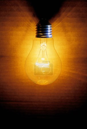 alte Glühbirne, ein Karton als Hintergrund wird beleuchtet, beleuchtet mit einem warmen gelben oder orangefarbenen Licht