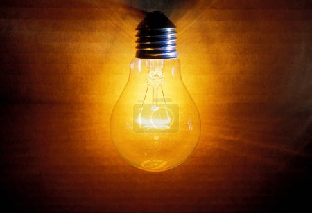 old burning light bulb, a carton as background is illuminated, lit with a warm yellow or orange light