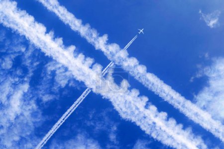 Ein Passagierflugzeug mit Kondensstreifen am blauen Himmel überquert andere Kondensstreifen