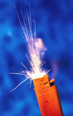 an orange-red lighter sprays sparks against a blue background