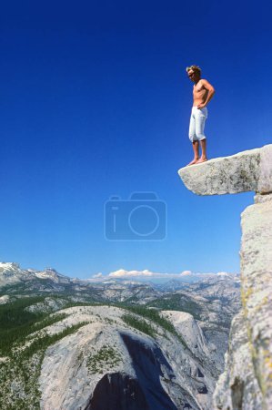 Ein Mann macht eine Mutprobe und steht auf einem Felsvorsprung auf der Spitze des Half Dome, 600 Meter über dem Boden, Yosemite Valley, Kalifornien, USA