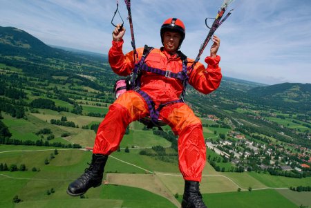 a man in signal red overalls in a paraglider high above the meadows near Lenggries, pilot's perspective, Bavaria, Germany