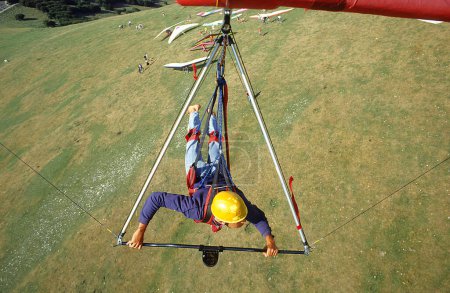 Du point de vue du pilote, un jeune homme pend dans un deltaplane et survole le site de lancement, où d'autres deltaplane peuvent être vus, Monte Cucco, Ombrie, Italie, Europe