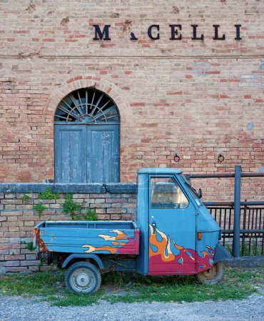 Via dei Macelli, Buonconvento, Tuscany, Italy, May 2009, a three-wheeled Pioggia Ape (Bee) transport car with painted flames stands in front of the slaughterhouses, Macelli means slaughterhouses