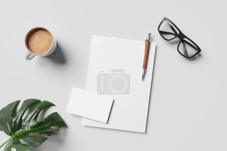Téléchargez les photos : Vue du dessus du lieu de travail avec papier blanc, stylo, lunettes, feuille et tasse à café sur fond gris - en image libre de droit