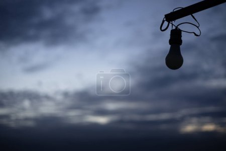 Photo for An image of an unlit light bulb against a  cloudy sky. - Royalty Free Image