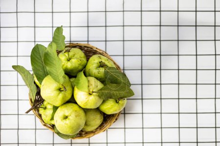 Draufsicht eine frische grüne rohe Guave. Früchte mit leuchtend grüner Rinde und weißem Fruchtfleisch, süß, knusprig in einem Bambuskorb isoliert auf weißem Hintergrund