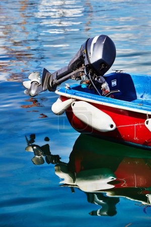 Photo for Isles of Scilly, United Kingdom - Detail of an outboard motor on a small boat floating in calm water in the port of Hugh Town, St.Marys. Reflection in Water. - Royalty Free Image