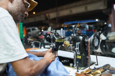 Photo for Delhi, India - October 19th 2019 - Indian man seaming a blue turban fabric witih an old sewing machine in a street shop in Delhi - Royalty Free Image