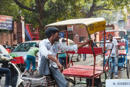 Téléchargez les photos : Delhi, Inde - 19 octobre 2019 - chauffeur indien de rikscha assis sur rikscha attendant les passagers sur une route animée à Delhi - en image libre de droit