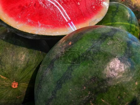 Nahaufnahme von süßen reifen Wassermelonen alias Citrullus lanatus Scheiben in einem Haufen grüner Wassermelonen zum Verkauf im Supermarkt.