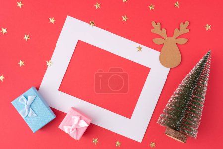 Creative concept of Christmas decorations, tree and gifts. Minimal layout on red background wtih copy space.