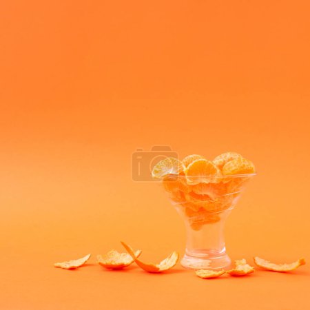 Foto de Rebanadas de naranja fresca pelada en una taza de vidrio sobre un fondo naranja. Diseño creativo. - Imagen libre de derechos
