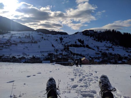 Schneebedeckte Berge, ein Spaziergang in einem Bergdorf. Foto.Schneebedeckte Berge mit hohen Fichten, Häuser eines Bergdorfes, Kinder im Hintergrund, strahlende Sonne und weiße Wolken.