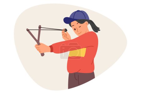 Little mischievous girl shoots with slingshot, closing one eye to aim at target during weekend. Child misbehaves by shooting at peers or glass with homemade slingshot with stretched rubber band.