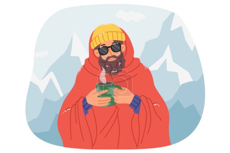 Man traveler drinks hot coffee, standing among snow-capped mountains after climbing to top. Traveler participating in winter hike is wrapped in warm blanket and holding mug with warming drink.