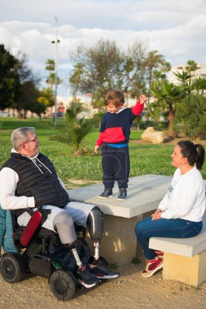 Der Sohn beansprucht die Aufmerksamkeit des Vaters im Rollstuhl vor den aufmerksamen Blicken der Mutter.